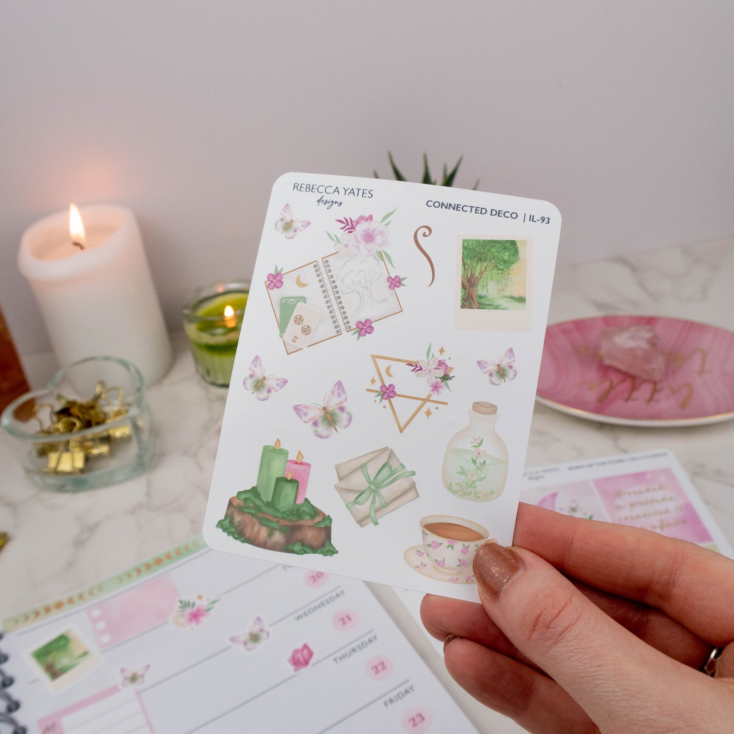 Earth Element Decorative Sticker Sheet with woodland scenes, tea cups, candles, butterflies, and greenery illustrations, displayed on a marble desk with a lit candle, planner, and decorative stationery items.