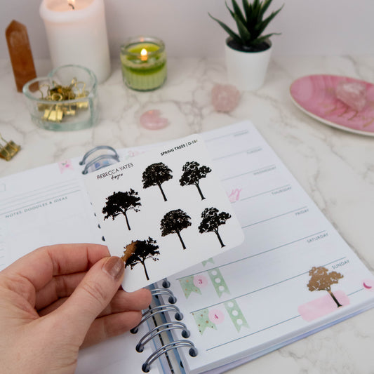 Small Spring Tree Sticker Sheet featuring six tree designs with gold foil accents, displayed on a marble desk with a lit candle and stationery.