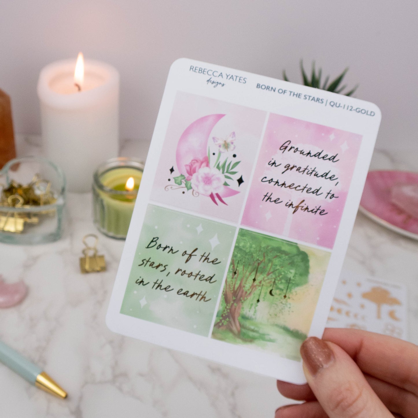 Born of the Stars Gold Foiled Sticker Sheet featuring two inspirational quotes and two gold-foiled illustrations, including a pink moon with flowers and a woodland scene, displayed on a marble desk with a lit candle and planner