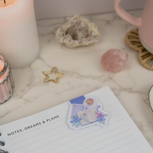 Close-up of a magnetic bookmark with a serene design of an open book, pastel flowers, and coffee, resting on a marble desk