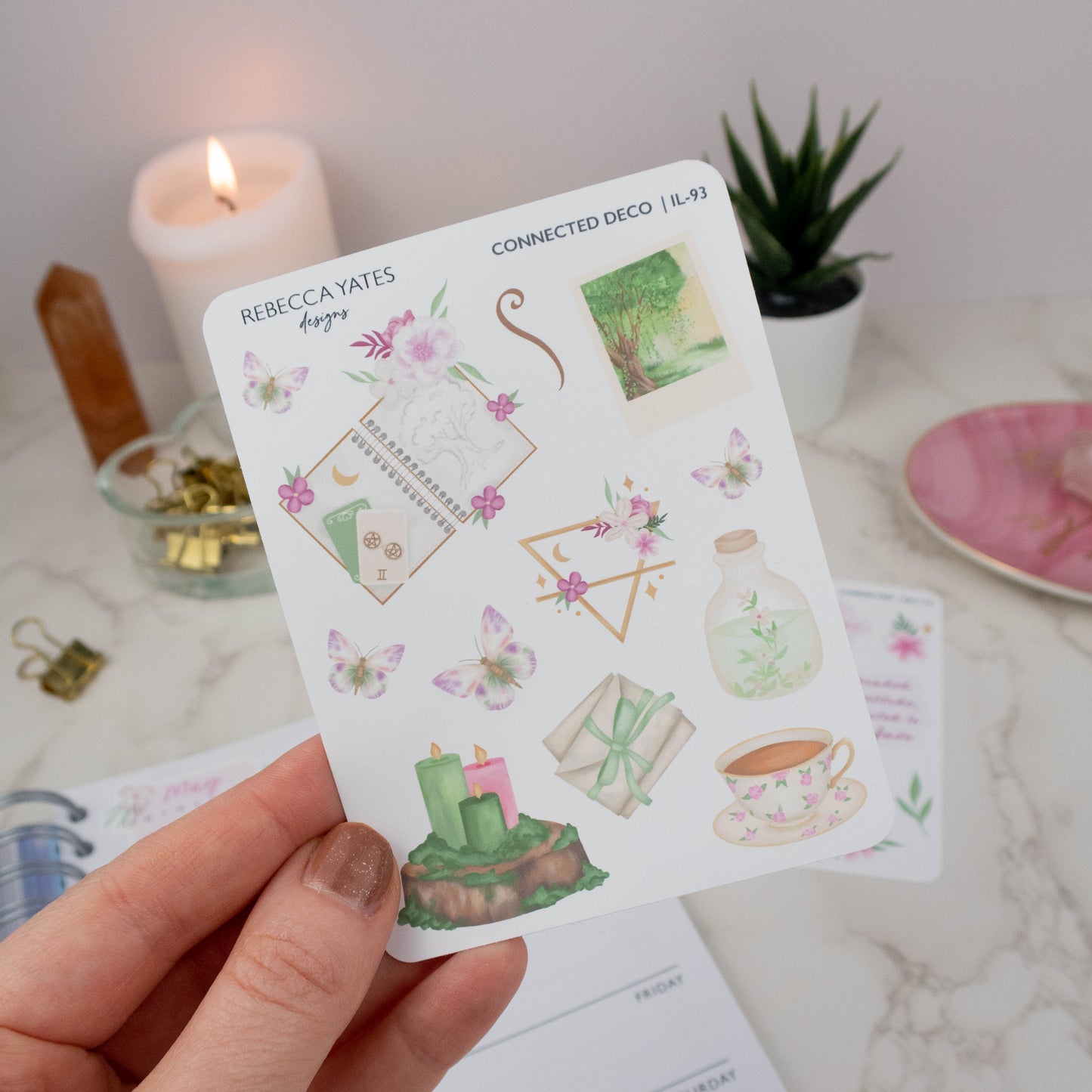 Earth Element Decorative Sticker Sheet with woodland scenes, tea cups, candles, butterflies, and greenery illustrations, displayed on a marble desk with a lit candle, planner, and decorative stationery items
