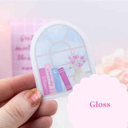 Hand holding a small round mirror with a decorative design on a light pink background
