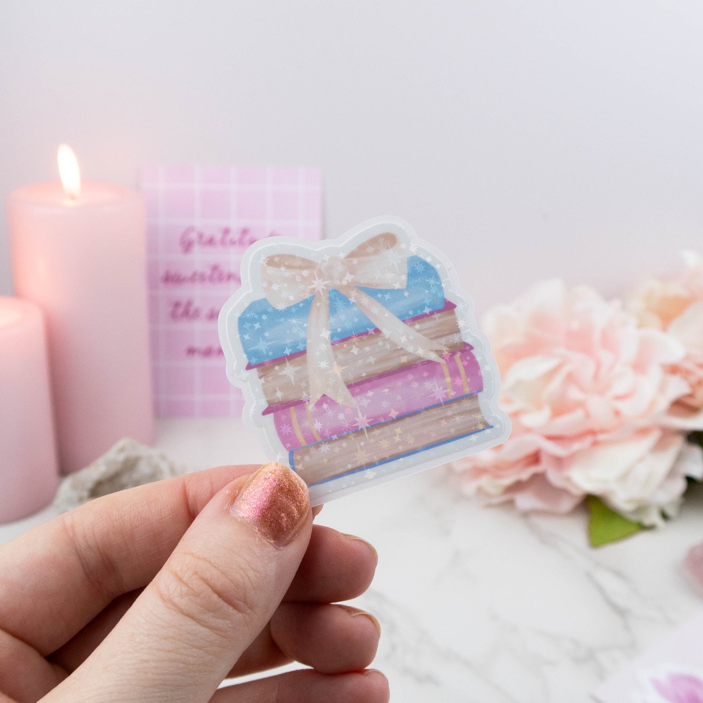 Hand holding a decorative sticker with a cake design, candles, and flowers in the background.