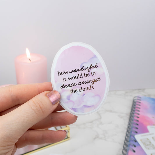 Hand holding a round sticker with a quote, with a candle and notebook in the background.