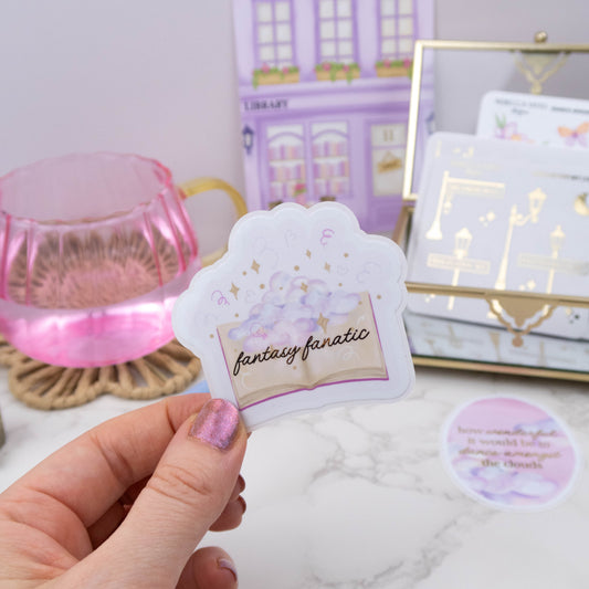 Hand holding a sticker with 'fantasy fanatic' text against a blurred background