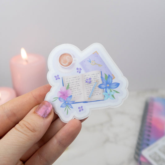 Heart-shaped decorative sticker with floral designs held by a hand against a neutral background