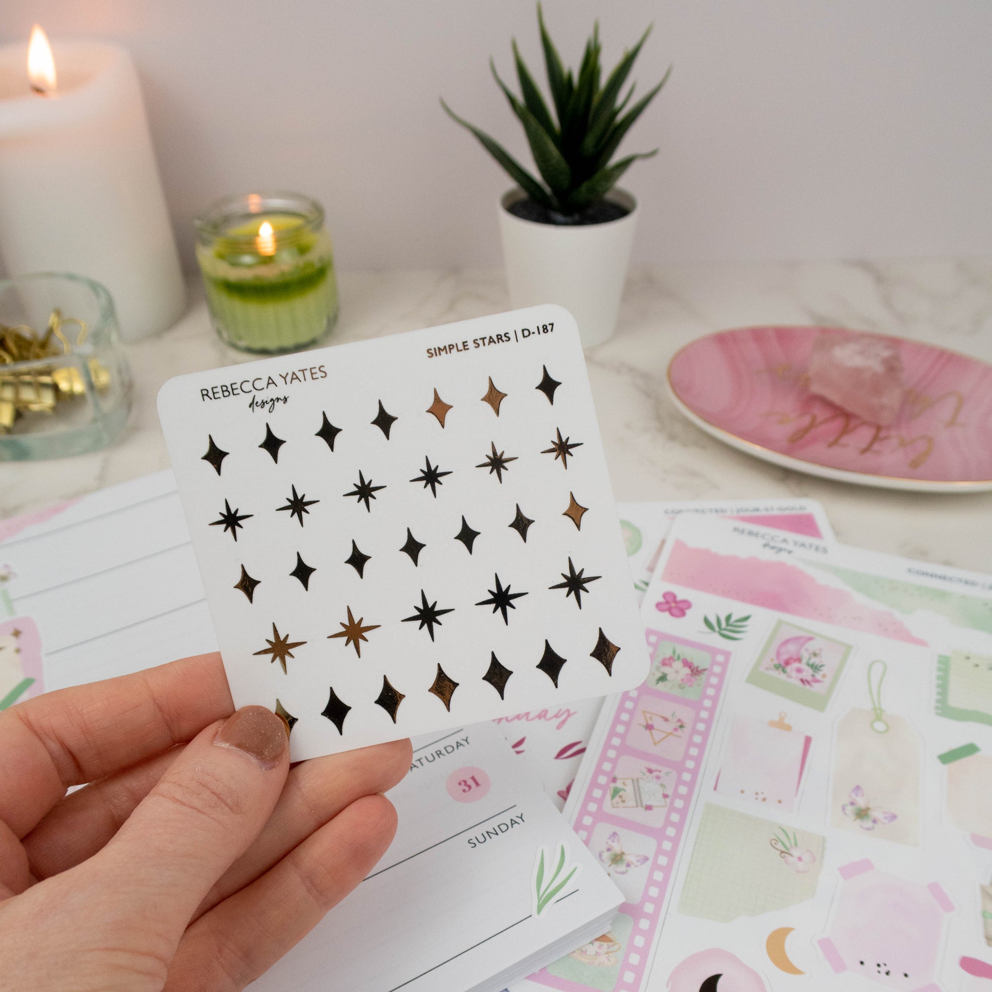 Elegant star stickers with shimmering foil accents, perfect for planners and bullet journals, displayed alongside a lit candle and stationery items.