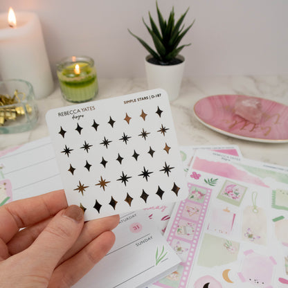 Elegant star stickers with shimmering foil accents, perfect for planners and bullet journals, displayed alongside a lit candle and stationery items.