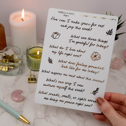 oiled Journal Prompts Sticker Sheet featuring reflective prompts with gold foil details, displayed on a marble desk with a lit candle and stationery