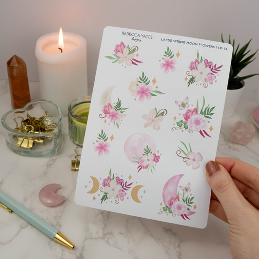 Large Spring Moon Flowers Decorative Sticker Sheet featuring pink flower and moon-themed illustrations, displayed on a marble desk with a planner, lit candle, and decorative stationery items