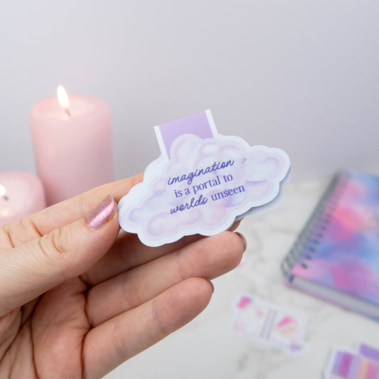 Hand holding a cloud-shaped sticker with text, candles in the background