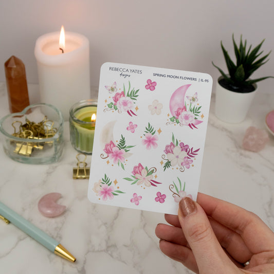 Spring Moon Flowers Decorative Sticker Sheet featuring pink flower and moon-themed illustrations, displayed on a marble desk with a planner, lit candle, and decorative stationery items