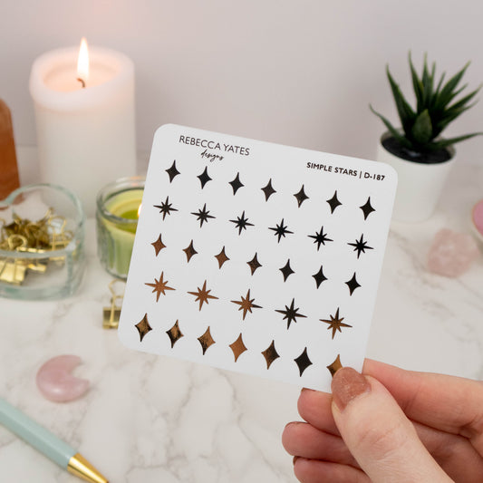 Simple Stars Sticker Sheet featuring 36 foiled star designs in gold, displayed on a marble desk with a lit candle and stationery.